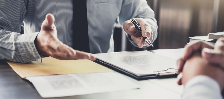 man sitting at desk gesturing towards paper on desk